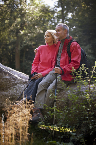 Photo: A mature couple sitting on a tree trunk resting A mature couple sitting on a tree trunk resting