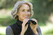 A mature woman outdoors, holding a pair of binoculars