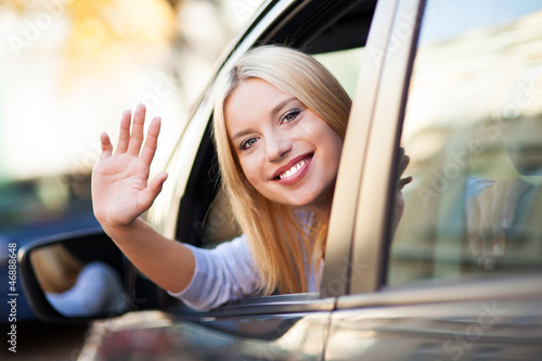 Photo: Young woman waving from car window Young woman waving from car window
