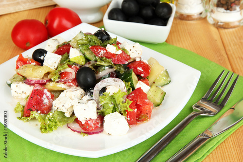 Photo: Fresh greek salad on plate on wooden table close-up Fresh greek salad on plate on wooden table close-up