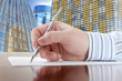 Businessman's Hand with Pen on the Office Buildings Background