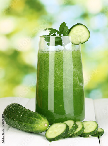Photo: Glass of cucumber juice on wooden table, on green background Glass of cucumber juice on wooden table, on green background