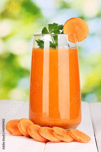Photo: Glass of carrot juice on wooden table, on green background Glass of carrot juice on wooden table, on green background