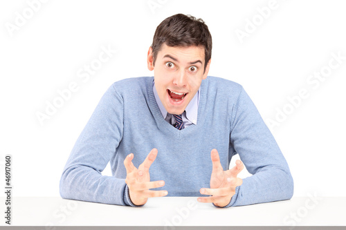 Photo: Angry young man sitting and gesturing with hands Angry young man sitting and gesturing with hands