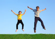 Boy and girl jump together at green grass at background of sky