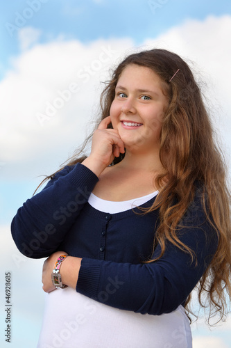 Photo: Beautiful smiling girl looks at camera at background of blue sky Beautiful smiling girl looks at camera at background of blue sky