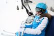 Two smiling female skiers in special clothing ride on cable car