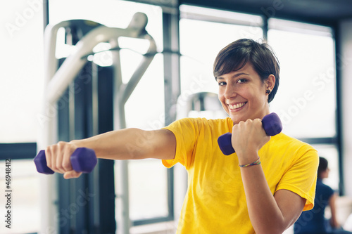 Photo: Young girl exercising with dumbbells in the gym. Young girl exercising with dumbbells in the gym.