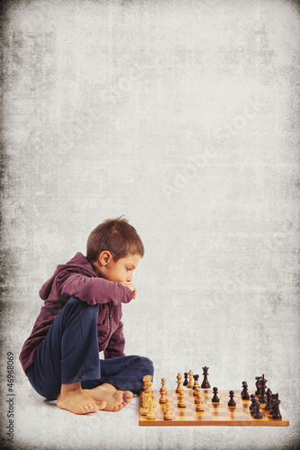 Photo: Kid (6 year old) playing chess, isolated on grunge background Kid (6 year old) playing chess, isolated on grunge background