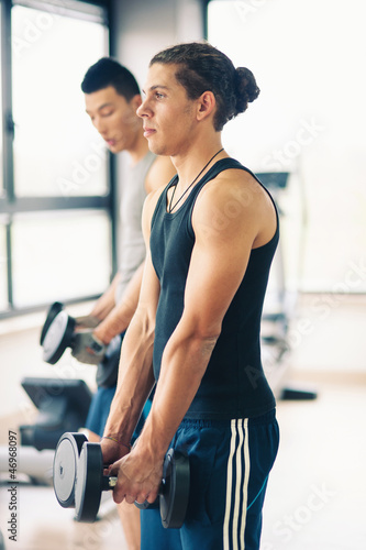 Photo: Two young men exercising with dumbbells in the gym. Two young men exercising with dumbbells in the gym.