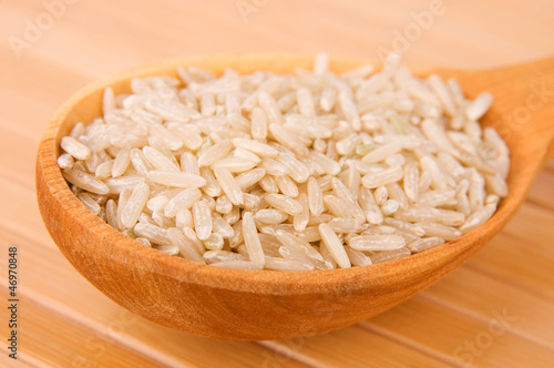 Photo: Raw brown rice in wooden spoon on bamboo close-up Raw brown rice in wooden spoon on bamboo close-up