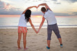 Romantic couple making heart shape with arms at sunset