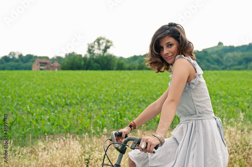 Photo: Beautiful young woman portrait with bike in a country road. Beautiful young woman portrait with bike in a country road.