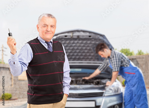 Photo: Mature gentleman holding a key while in the background mechanic Mature gentleman holding a key while in the background mechanic