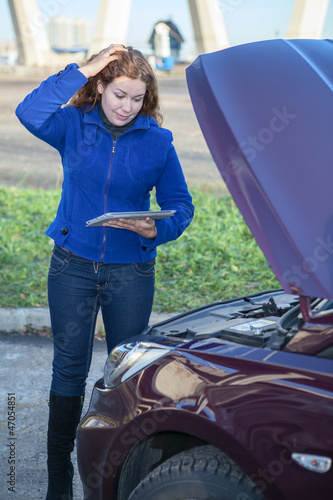 Photo: Woman in thought standing near car with tablet pc Woman in thought standing near car with tablet pc