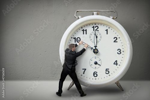 Photo: Businessman pulling a clock hand backwards Businessman pulling a clock hand backwards