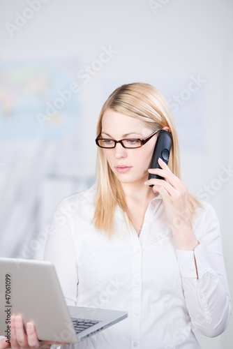 Photo: junge frau im büro mit telefon und laptop junge frau im büro mit telefon und laptop