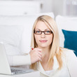 blonde frau sitzt mit laptop auf dem sofa