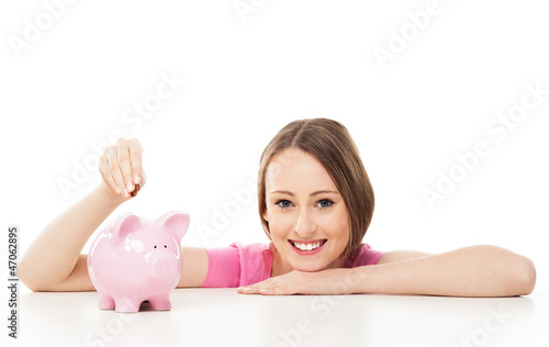 Photo: Young woman putting money in piggy bank Young woman putting money in piggy bank