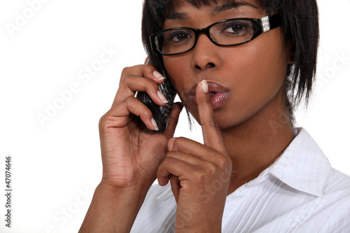Photo: Black businesswoman making hush gesture during phone call Black businesswoman making hush gesture during phone call