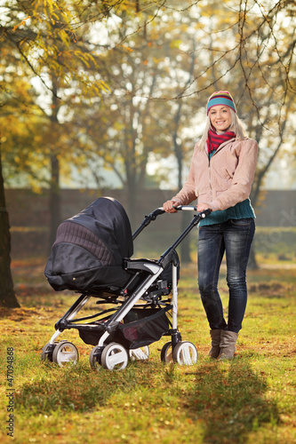 Photo: A smiling mother posing with a baby stroller in autumn A smiling mother posing with a baby stroller in autumn