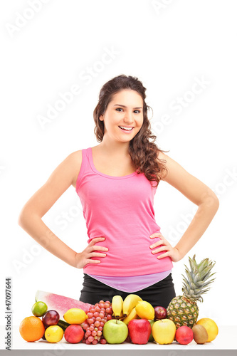 Photo: Young female athlete posing behind a pile of different fruits Young female athlete posing behind a pile of different fruits