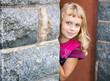 Little girl looks out from behind the wall and smiles