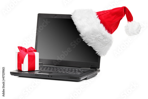 Photo: Studio shot of santa hat and gift on a laptop Studio shot of santa hat and gift on a laptop