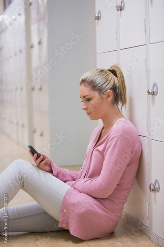 Photo: Woman sitting against locker texting Woman sitting against locker texting