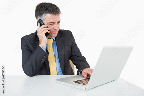 Photo: Man phoning while writing on laptop Man phoning while writing on laptop