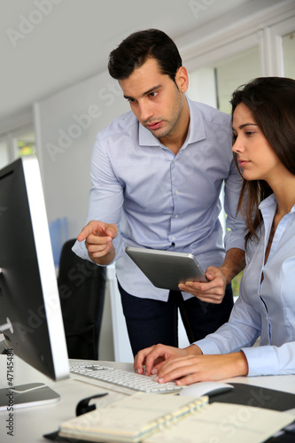 Photo: Office workers in front of desktop computer with tablet Office workers in front of desktop computer with tablet