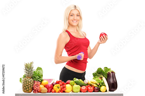 Photo: Female athlete holding a dumbbell and apple behind a pile of foo Female athlete holding a dumbbell and apple behind a pile of foo