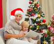 Photo: Happy mother and baby using tablet PC near Christmas tree Happy mother and baby using tablet PC near Christmas tree