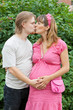 a happy young pregnant woman with her husband kissing in a park