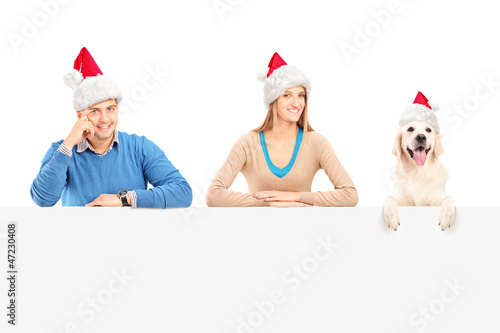 Photo: Smiling couple and dog with santa hats posing behind a panel Smiling couple and dog with santa hats posing behind a panel