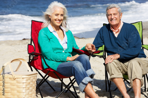 Photo: Senior Couple Sitting On Beach In Deckchairs Having Picnic Senior Couple Sitting On Beach In Deckchairs Having Picnic