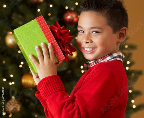 Photo: Boy Holding Christmas Present In Front Of Tree Boy Holding Christmas Present In Front Of Tree