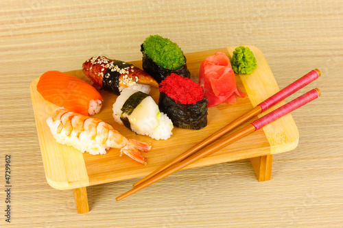 Photo: delicious sushi served on wooden board on bamboo mat delicious sushi served on wooden board on bamboo mat
