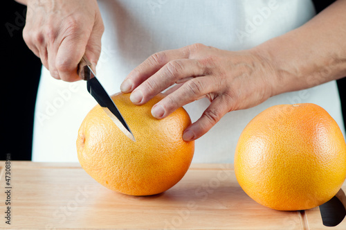 Photo: Female hands cutting a grapefruit, horizontal shot Female hands cutting a grapefruit, horizontal shot