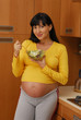 Mujer embarazada comiendo ensalada de vegetales en la cocina