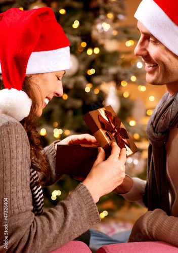 Photo: Christmas Scene. Happy Couple with Christmas Gift at Home Christmas Scene. Happy Couple with Christmas Gift at Home