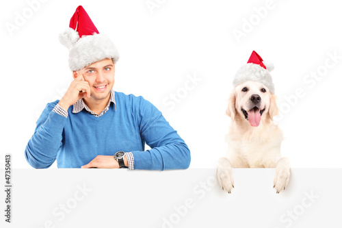 Photo: Smiling guy and dog wearing santa claus hats and posing behind a Smiling guy and dog wearing santa claus hats and posing behind a