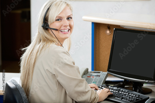 Photo: Cheerful Woman Using Computer At Reception Desk Cheerful Woman Using Computer At Reception Desk