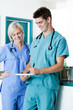 Male Doctor Writing On Clipboard With Colleague At Clinic