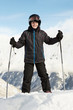 Boy in ski suit stands leaning on ski poles with blue sky