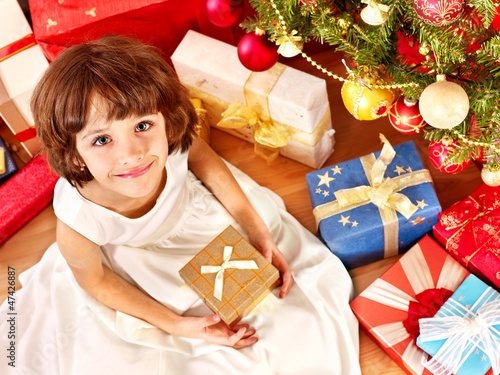 Photo: Child with gift box near Christmas tree. Child with gift box near Christmas tree.
