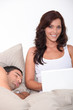 woman having fun on her laptop while her husband is sleeping