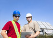 two contractors holding tablet pc and standing before solar pane