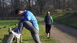 Man stretching, woman jogging in park, crane shot