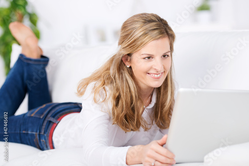 Foto: blonde frau liegt mit laptop auf dem sofa blonde frau liegt mit laptop auf dem sofa
